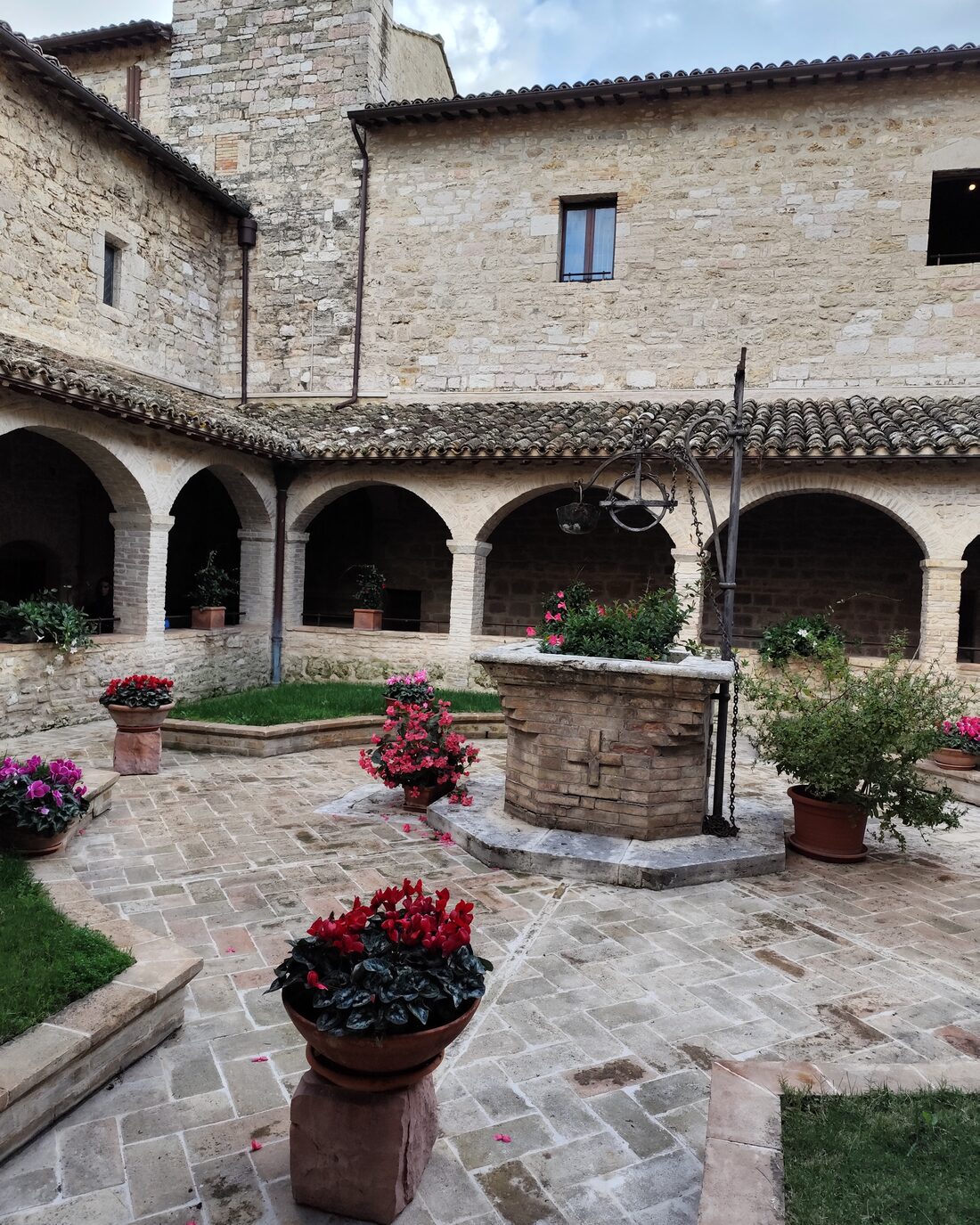 A stone cloister with a well and pots of flowers