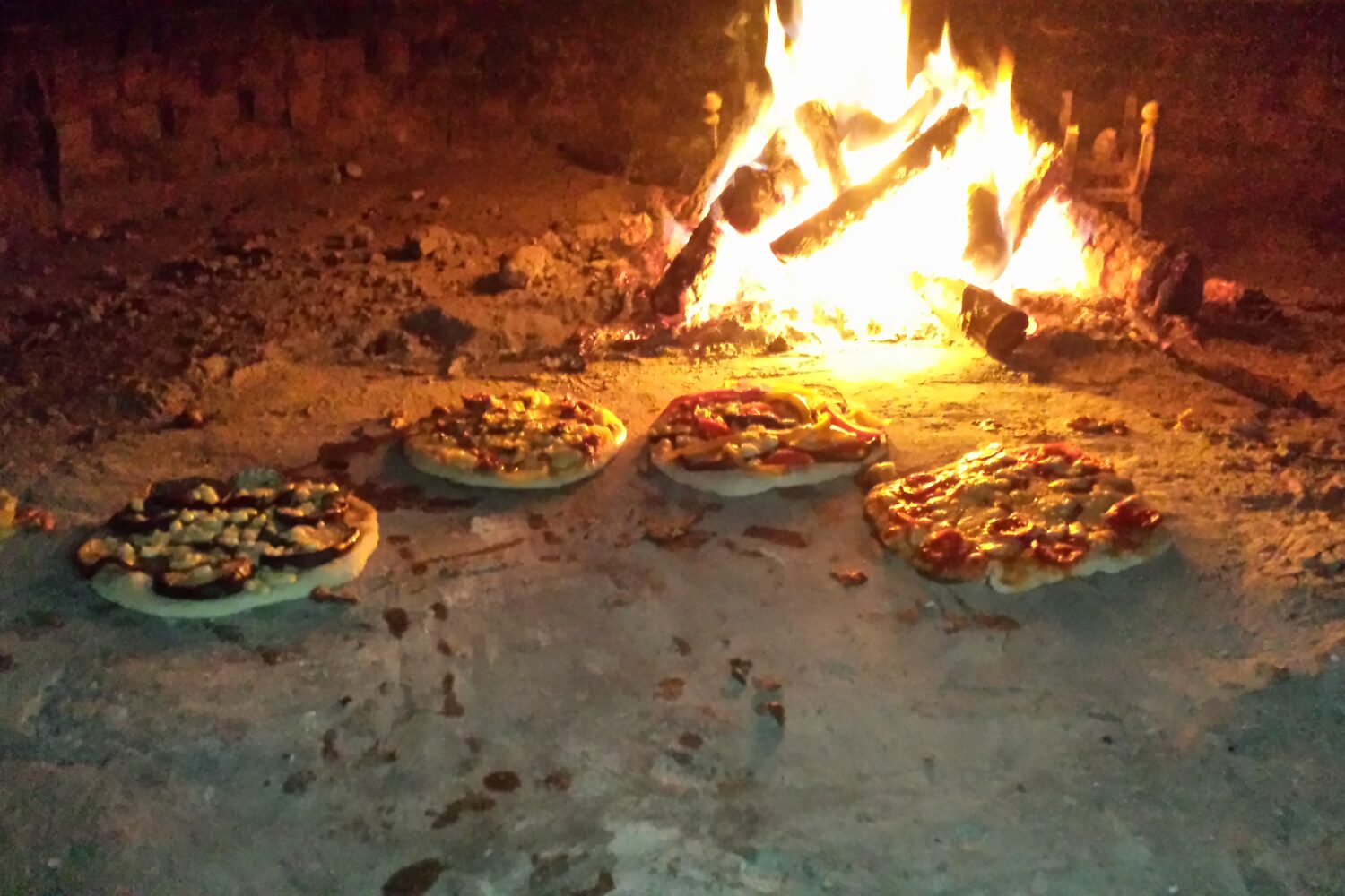 Pizzas baking inside a lit wood-fired oven
