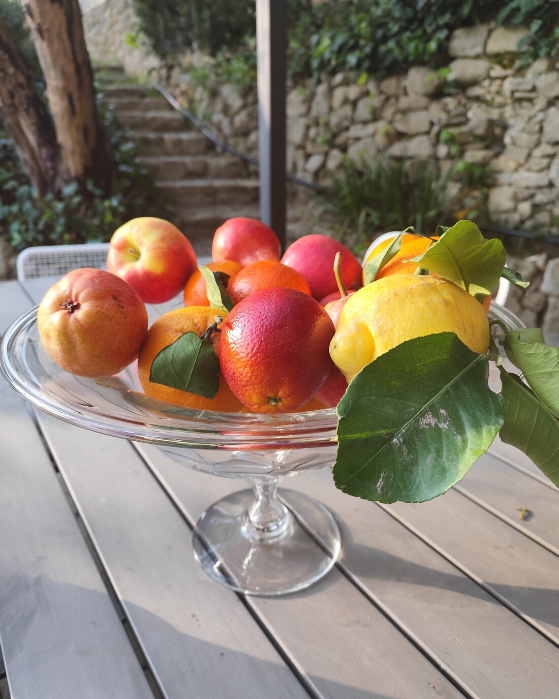 A glass stand of seasonal fruit on a garden table