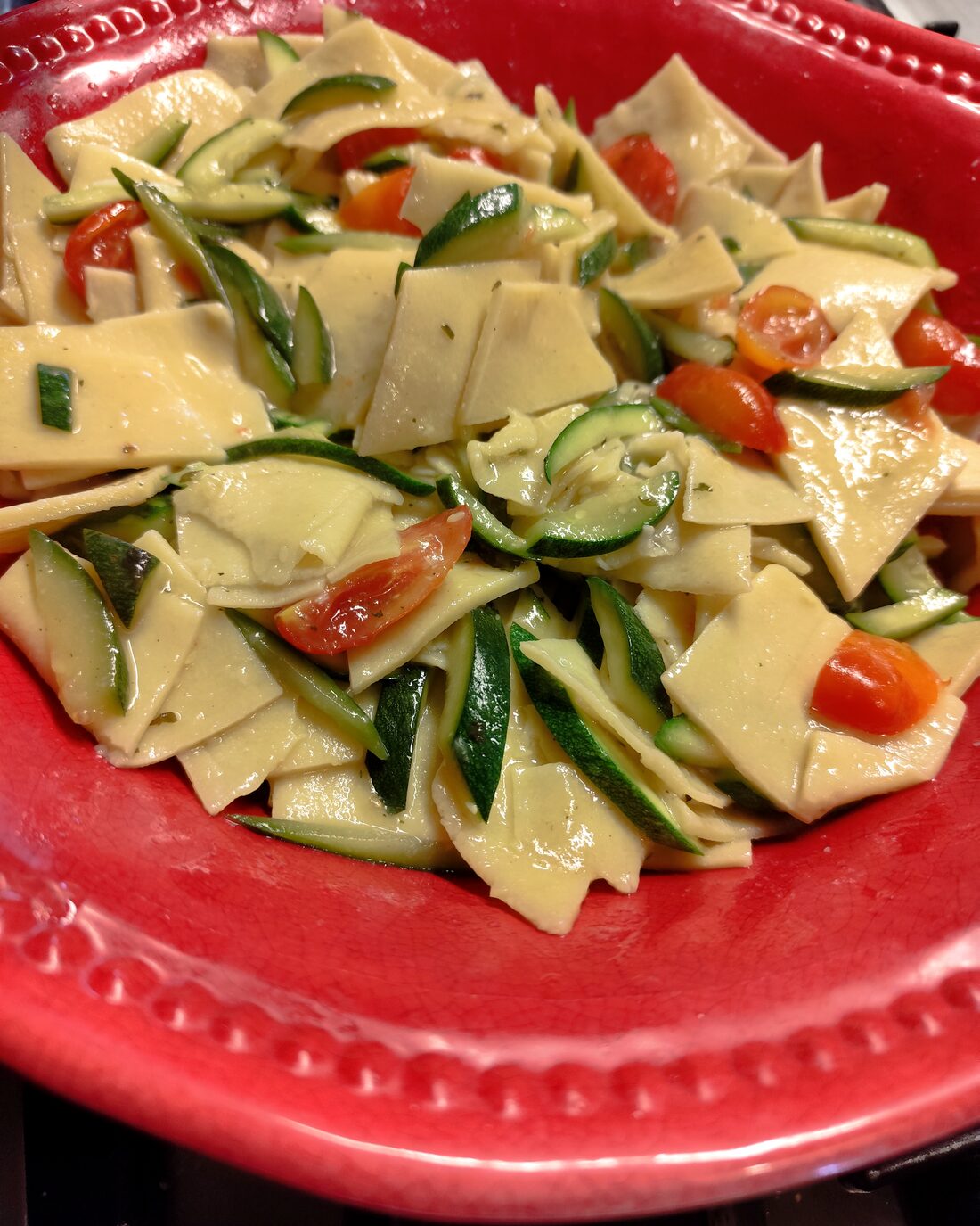 Fresh pasta with courgettes and cherry tomatoes on a red plate