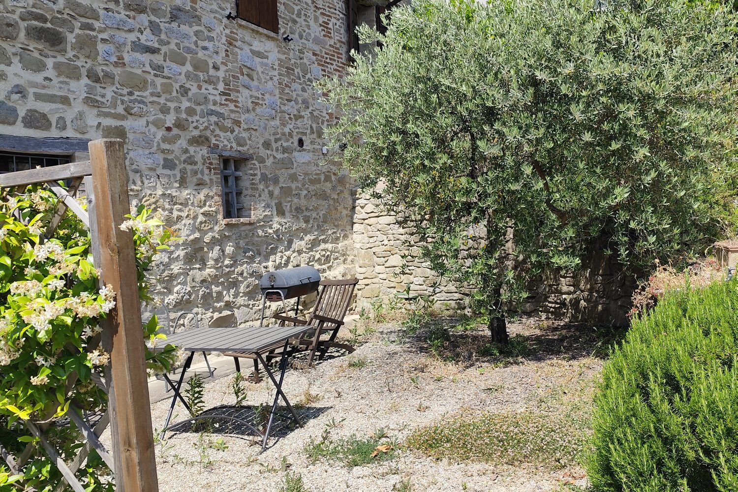 Il retro di una casa in pietra umbra, con un olivo e un tavolino in giardino
